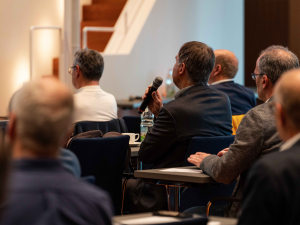 Nahaufnahme des Publikums von hinten bei der microTEC Clusterkonferenz 2023. Ein Teilnehmer stellt gerade eine Frage und hält deshalb ein Mikrofon in der Hand.