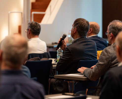 microTEC Südwest Clusterkonferenz 2023 Tag 1 (15) Nahaufnahme des Publikums von hinten bei der microTEC Clusterkonferenz 2023. Ein Teilnehmer stellt gerade eine Frage und hält deshalb ein Mikrofon in der Hand.